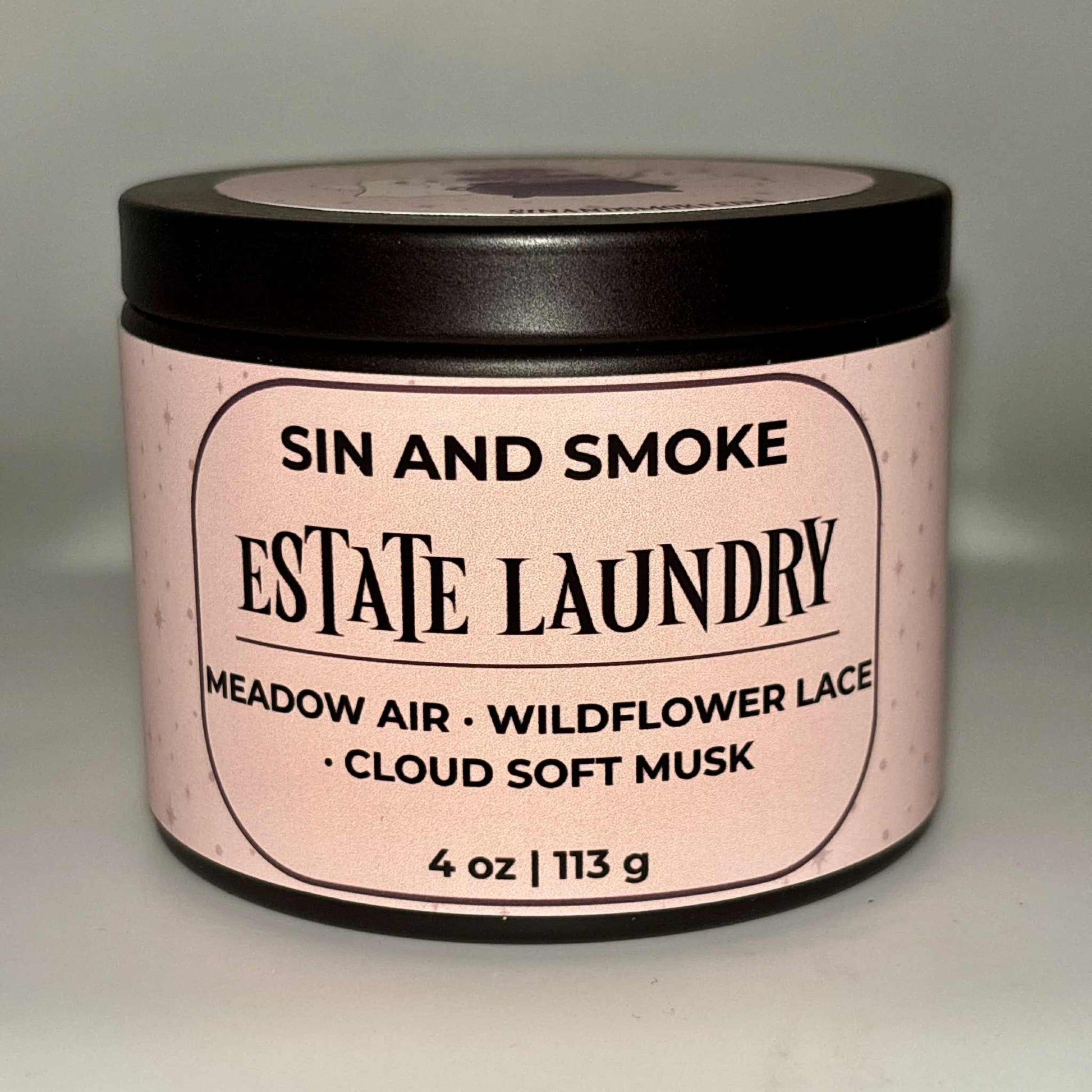 Sin and Smoke Estate Laundry candle in a soft pink jar with clean fresh linen inspired scent notes meadow air wildflower lace and cloud soft musk